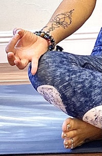 a woman sitting in a yoga pose with a tattoo on her arm